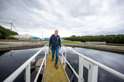 Medewerker loopt over brug bij waterzuiveringsinstallatie